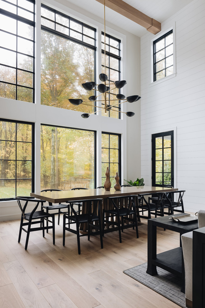 Dining Area - Large open-concept dining room featuring a black and gold chandelier, wood dining table, mid-century dining chairs, hardwood flooring, black windows, and shiplap walls.