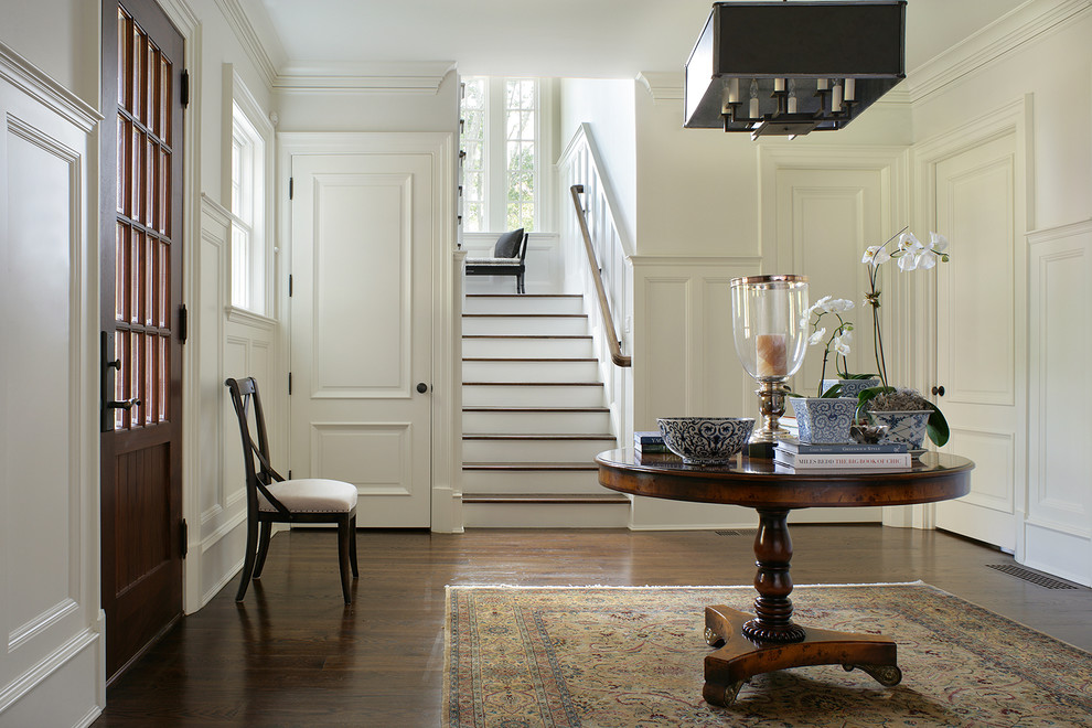 This is an example of a large traditional foyer in New York with white walls, dark hardwood floors, a single front door and a dark wood front door.
