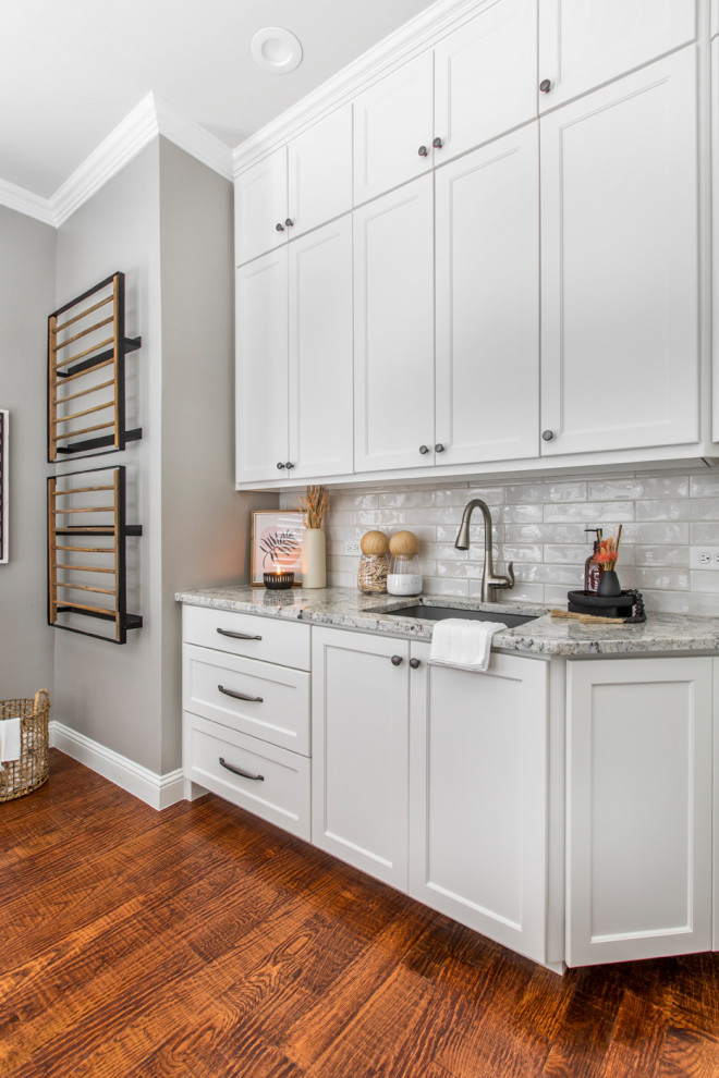 This is an example of a mid-sized traditional dedicated laundry room in Dallas with an undermount sink, shaker cabinets, white cabinets, granite benchtops, white splashback, subway tile splashback, grey walls, vinyl floors, a side-by-side washer and dryer, brown floor and grey benchtop.