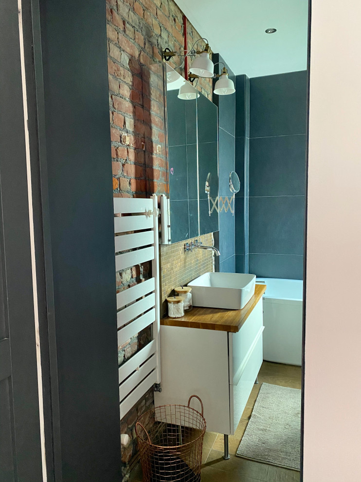 This is an example of a small scandi ensuite bathroom in Lille with white cabinets, a freestanding bath, a shower/bath combination, grey tiles, ceramic tiles, grey walls, wood-effect flooring, a vessel sink, wooden worktops, brown floors, an open shower, a single sink, a freestanding vanity unit and brick walls.