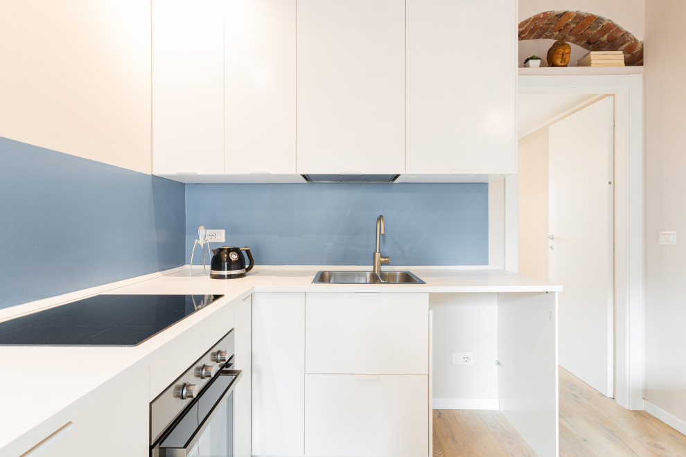 Foto på ett litet skandinaviskt vit kök, med en dubbel diskho, släta luckor, vita skåp, laminatbänkskiva, blått stänkskydd och ljust trägolv