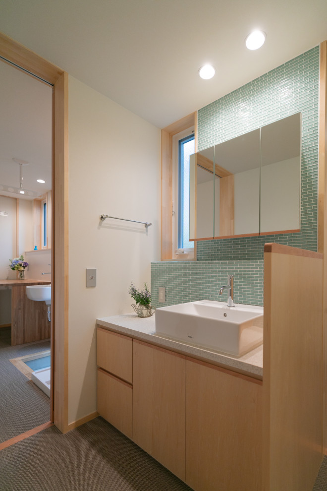 他の地域にあるお手頃価格の中くらいなコンテンポラリースタイルのおしゃれなトイレ・洗面所 (インセット扉のキャビネット、茶色いキャビネット、壁掛け式トイレ、緑のタイル、ガラスタイル、白い壁、クッションフロア、ベッセル式洗面器、木製洗面台、ベージュの床、白い洗面カウンター、独立型洗面台、クロスの天井、壁紙) の写真