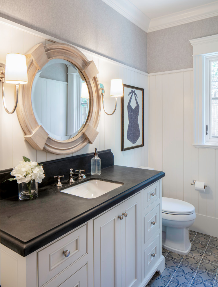 Photo of a mid-sized beach style 3/4 bathroom in San Francisco with beaded inset cabinets, white cabinets, a one-piece toilet, white walls, mosaic tile floors, an undermount sink, granite benchtops, grey floor, black benchtops, an enclosed toilet, a single vanity, a built-in vanity and decorative wall panelling.