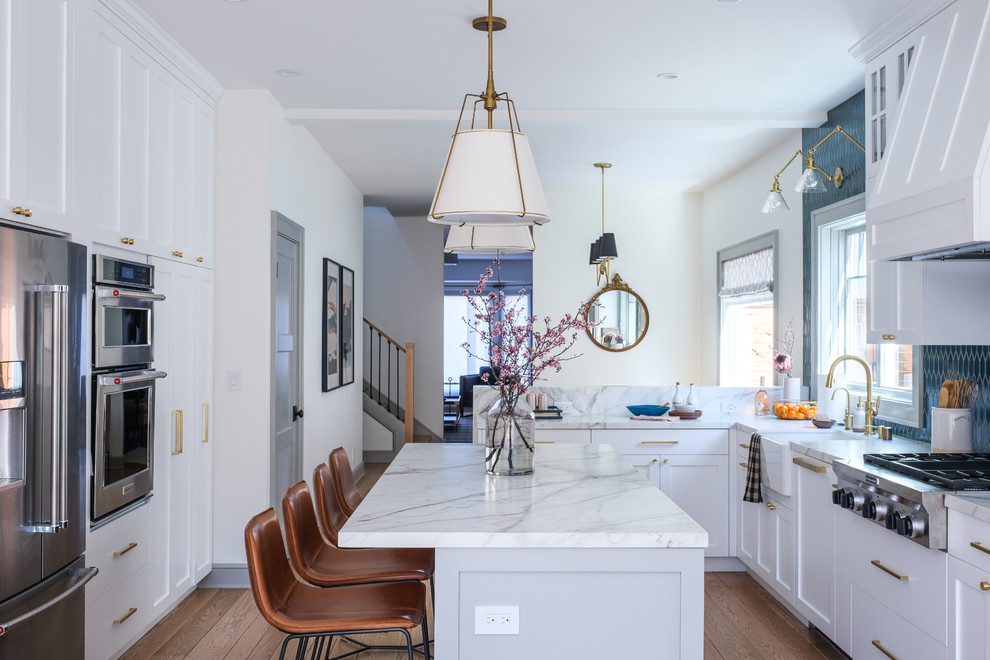 Mid-sized transitional u-shaped medium tone wood floor and brown floor kitchen photo in San Francisco with a farmhouse sink, shaker cabinets, marble countertops, blue backsplash, stainless steel appliances, an island, white countertops and white cabinets