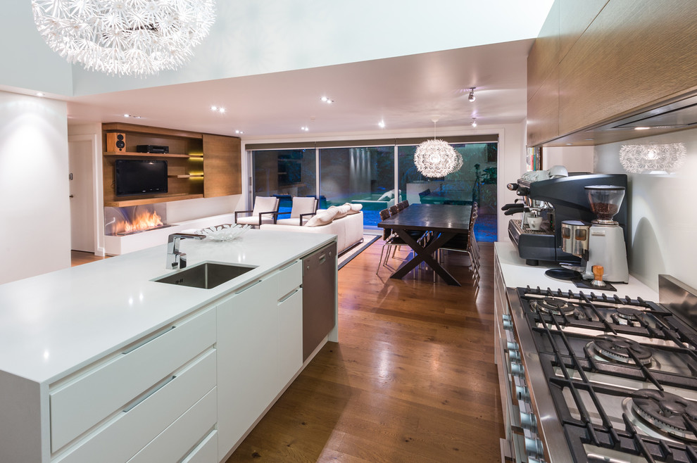 Photo of a contemporary galley open plan kitchen in Auckland with an undermount sink, flat-panel cabinets, quartz benchtops, white splashback, glass sheet splashback, stainless steel appliances and white cabinets.