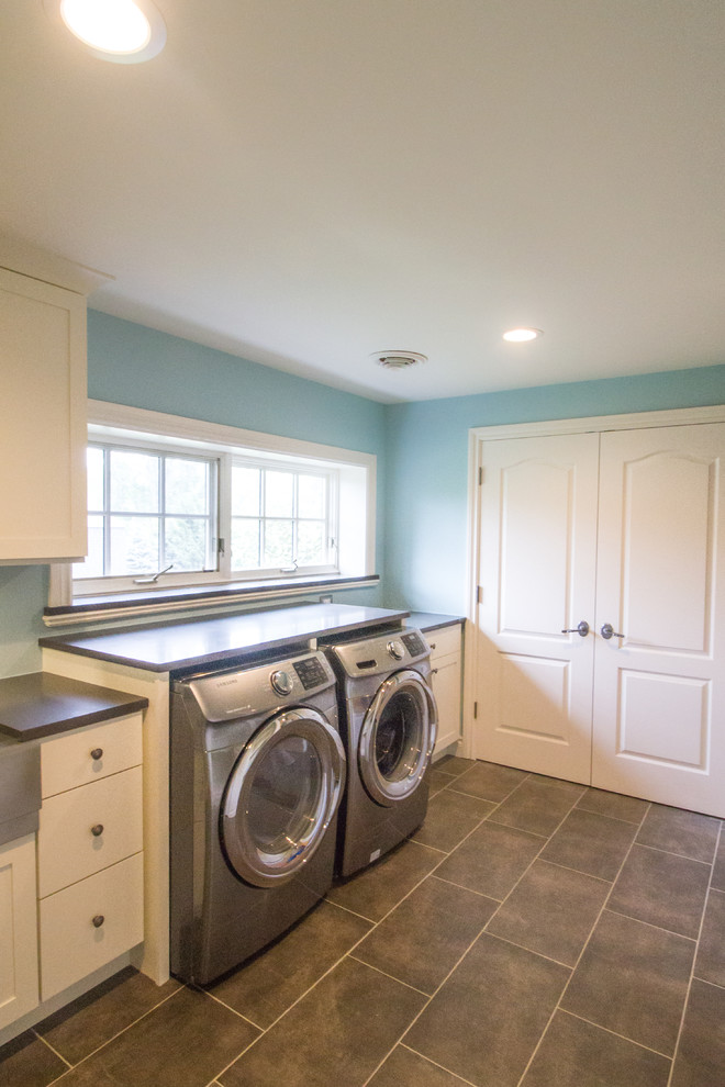 Design ideas for a mid-sized transitional single-wall dedicated laundry room in Detroit with a farmhouse sink, shaker cabinets, white cabinets, soapstone benchtops, blue walls, ceramic floors and a side-by-side washer and dryer.