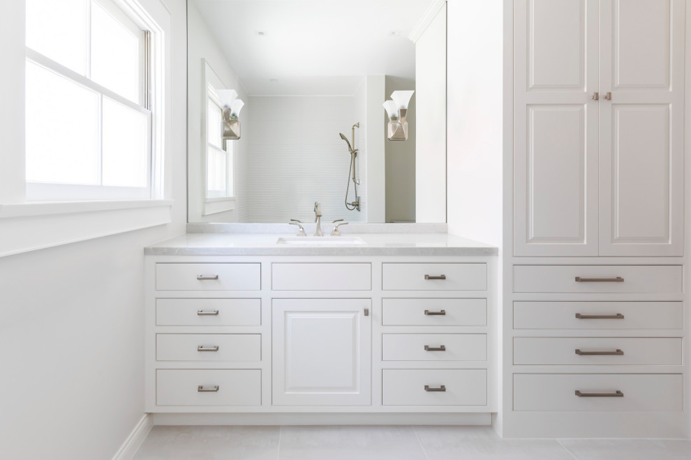 Photo of a mid-sized contemporary bathroom in Los Angeles with beaded inset cabinets, white cabinets, an alcove tub, a shower/bathtub combo, a two-piece toilet, white tile, porcelain tile, white walls, porcelain floors, an undermount sink, engineered quartz benchtops, grey floor, a shower curtain, white benchtops and a single vanity.