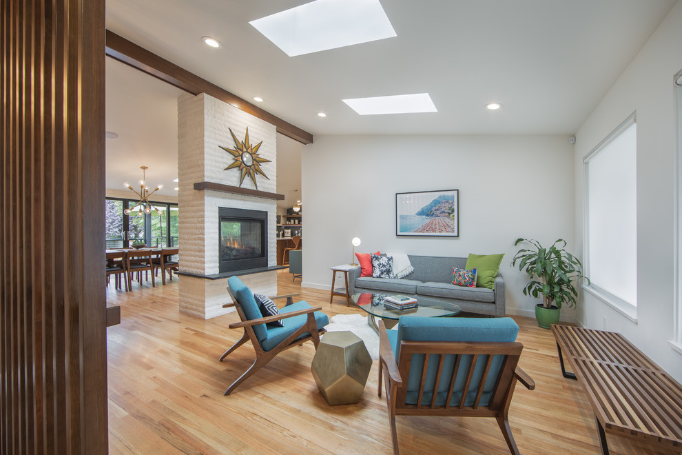 Midcentury living room in Seattle with medium hardwood floors, a two-sided fireplace, a brick fireplace surround and vaulted.