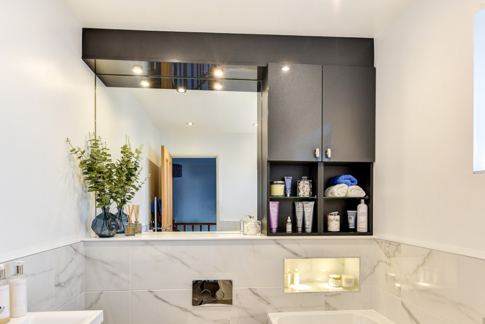 Inspiration for a small modern grey and white family bathroom in Sussex with flat-panel cabinets, grey cabinets, a built-in bath, a shower/bath combination, a wall mounted toilet, white tiles, marble tiles, white walls, laminate floors, an integrated sink, marble worktops, brown floors, a shower curtain, a wall niche, a single sink and a built in vanity unit.