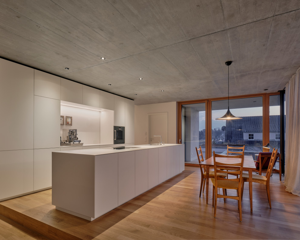 Modern kitchen in Stuttgart with flat-panel cabinets, white cabinets, laminate countertops, white splashback, medium hardwood flooring, an island, brown floors and white worktops.