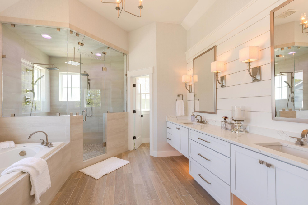 This is an example of a beach style bathroom in Other with shaker cabinets, white cabinets, a drop-in tub, a corner shower, grey walls, an undermount sink, brown floor, a hinged shower door, white benchtops and a double vanity.
