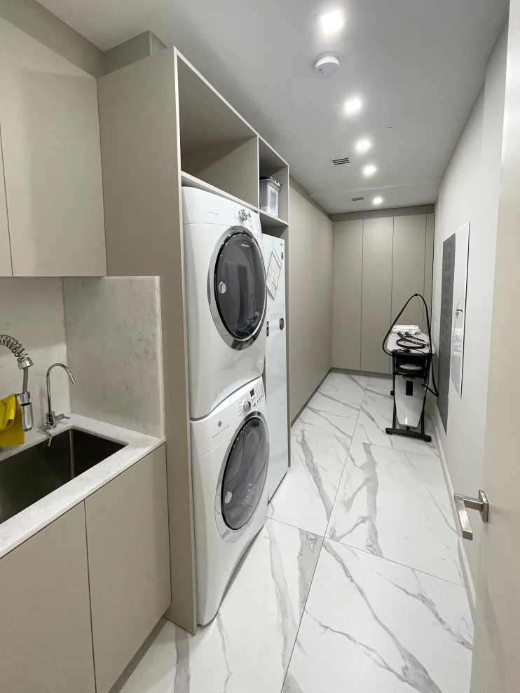 Design ideas for a medium sized classic galley utility room in Miami with a submerged sink, flat-panel cabinets, grey cabinets, quartz worktops, white splashback, stone slab splashback, beige walls, porcelain flooring, a stacked washer and dryer, white floors and white worktops.