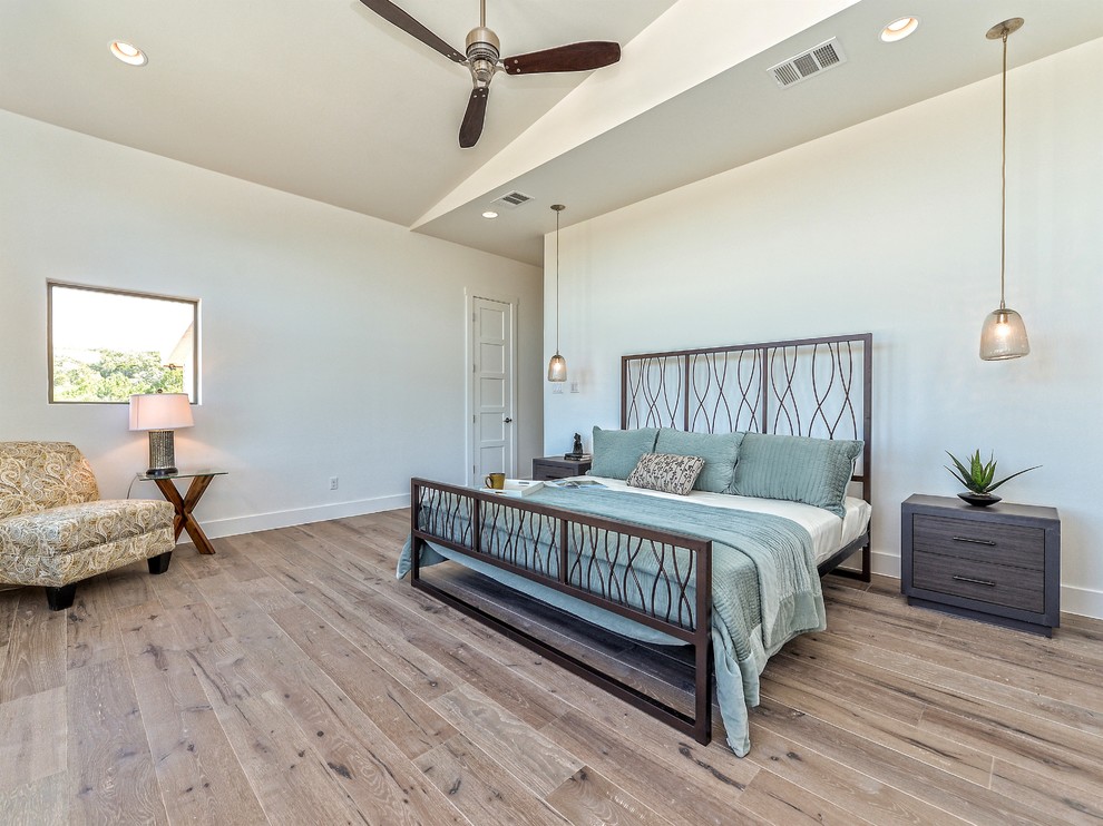 This is an example of a large transitional master bedroom in Austin with white walls, light hardwood floors, no fireplace and brown floor.