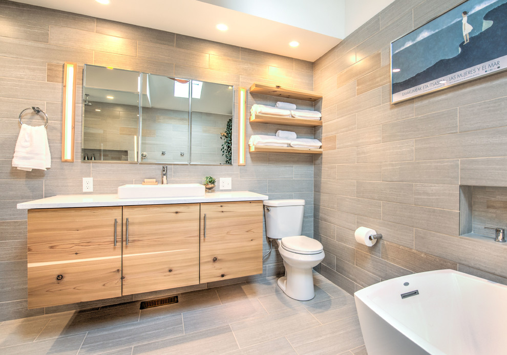 Design ideas for a large modern master bathroom in Other with flat-panel cabinets, light wood cabinets, a freestanding tub, a curbless shower, a two-piece toilet, gray tile, ceramic tile, white walls, ceramic floors, a vessel sink, engineered quartz benchtops, grey floor and an open shower.
