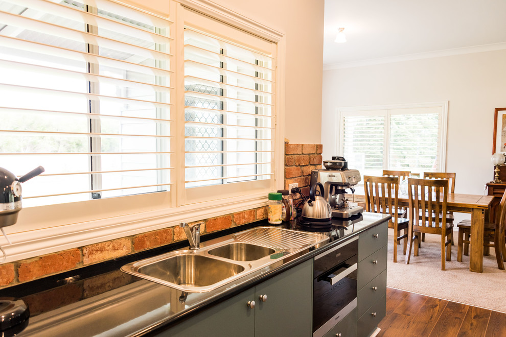 This is an example of a small country galley kitchen pantry in Geelong with a double-bowl sink, green cabinets, laminate benchtops, red splashback, brick splashback, stainless steel appliances, linoleum floors, with island and brown floor.