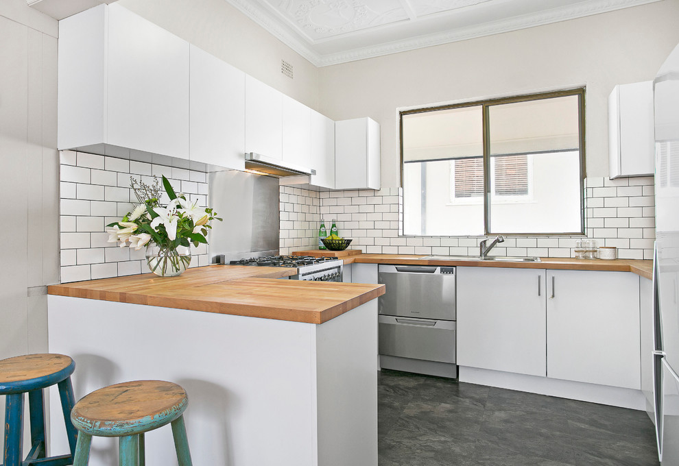 Mid-sized contemporary u-shaped separate kitchen in Sydney with a double-bowl sink, white cabinets, wood benchtops, white splashback, subway tile splashback, stainless steel appliances, vinyl floors, flat-panel cabinets and a peninsula.