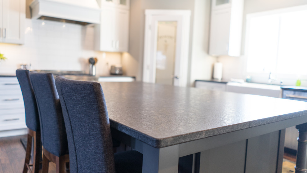Example of a large transitional u-shaped eat-in kitchen design with a farmhouse sink, flat-panel cabinets, white cabinets, granite countertops, white backsplash, ceramic backsplash, stainless steel appliances and an island