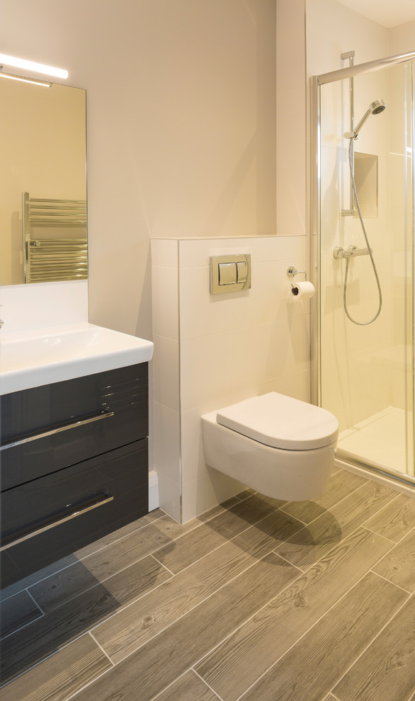 This is an example of a small transitional master bathroom in Dublin with an open shower, a wall-mount toilet, white tile, porcelain tile, white walls, porcelain floors, brown floor and a sliding shower screen.
