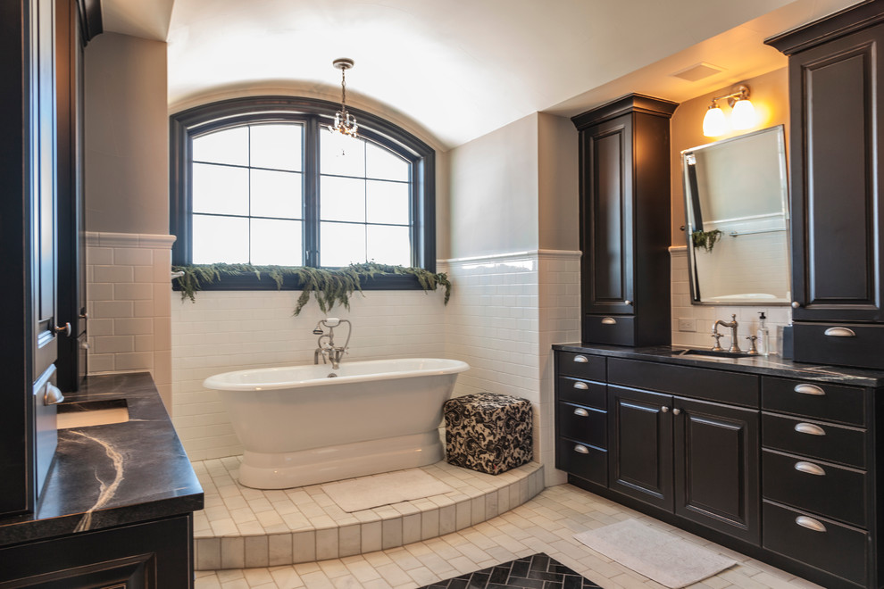 Example of a transitional white tile and subway tile porcelain tile freestanding bathtub design in Denver with a farmhouse sink, raised-panel cabinets, soapstone countertops, white backsplash, subway tile backsplash, stainless steel appliances, an island, dark wood cabinets, gray walls and an undermount sink