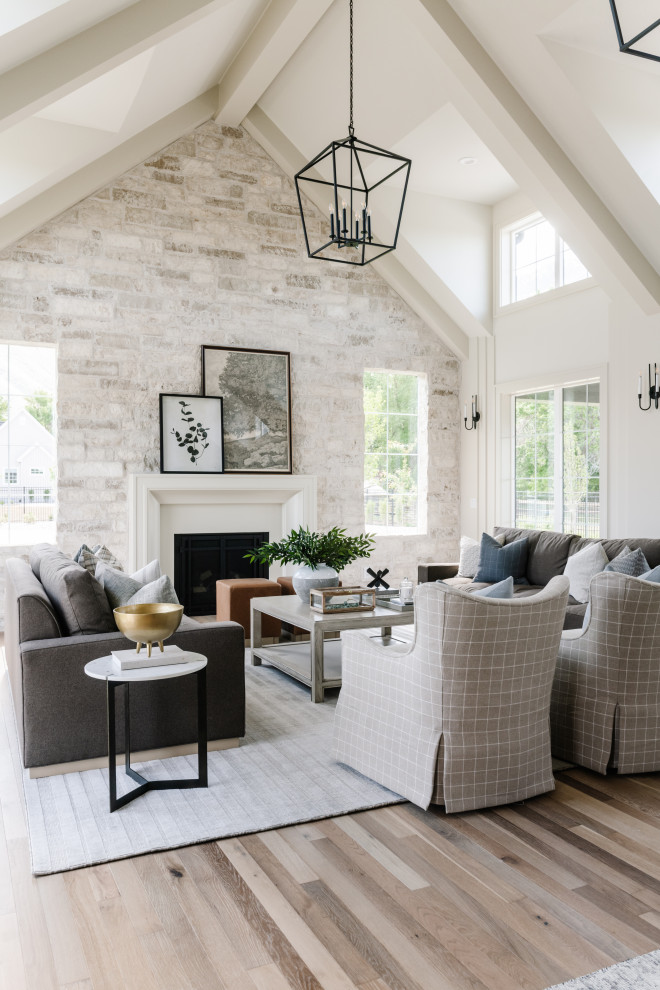 This is an example of a transitional open concept living room in Salt Lake City with white walls, light hardwood floors, a standard fireplace, beige floor, exposed beam, vaulted and brick walls.