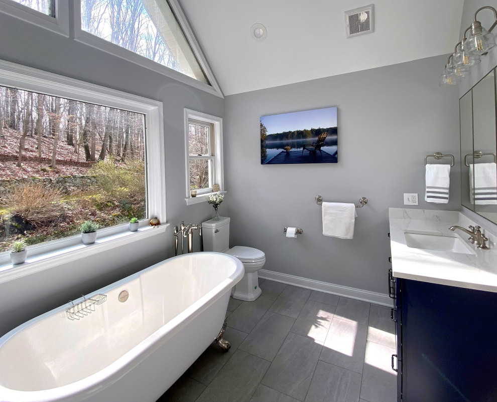 This is an example of a large transitional master bathroom in Philadelphia with shaker cabinets, blue cabinets, gray tile, engineered quartz benchtops, white benchtops, a built-in vanity, a claw-foot tub, a corner shower, a one-piece toilet, subway tile, grey walls, ceramic floors, an undermount sink, grey floor, a hinged shower door and a double vanity.