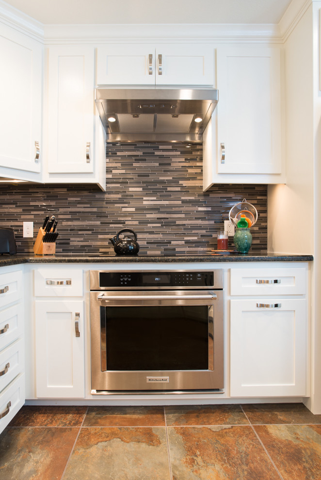 Photo of a small transitional u-shaped separate kitchen in Dallas with an undermount sink, shaker cabinets, white cabinets, granite benchtops, multi-coloured splashback, glass tile splashback, stainless steel appliances, porcelain floors and no island.
