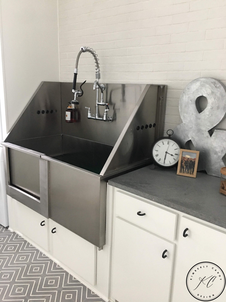 Inspiration for a small eclectic galley utility room in Omaha with a drop-in sink, flat-panel cabinets, white cabinets, quartz benchtops, white splashback, ceramic splashback, white walls, concrete floors, a stacked washer and dryer, grey floor and grey benchtop.