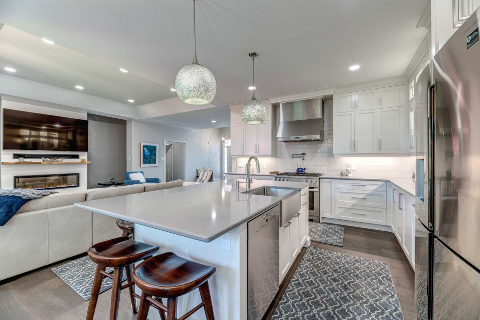 Eat-in kitchen - transitional l-shaped eat-in kitchen idea with a farmhouse sink, shaker cabinets, white cabinets, quartz countertops, porcelain backsplash, stainless steel appliances, an island and white countertops