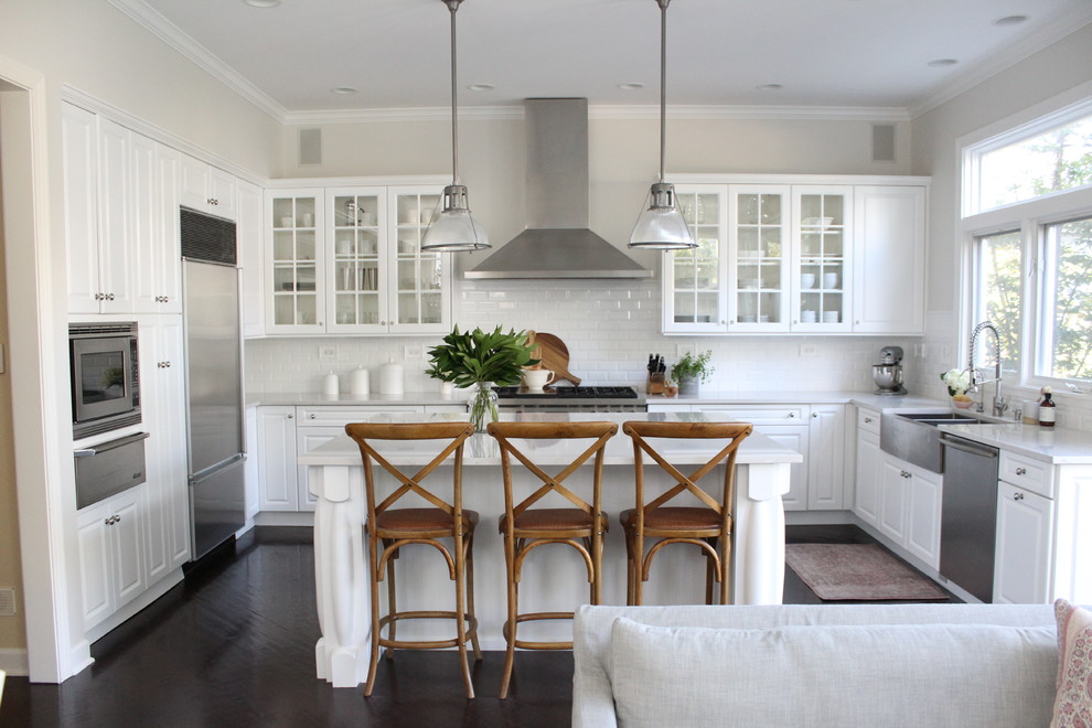 Design ideas for a large transitional u-shaped eat-in kitchen in Chicago with a farmhouse sink, raised-panel cabinets, white cabinets, quartz benchtops, white splashback, ceramic splashback, stainless steel appliances, dark hardwood floors, with island and brown floor.