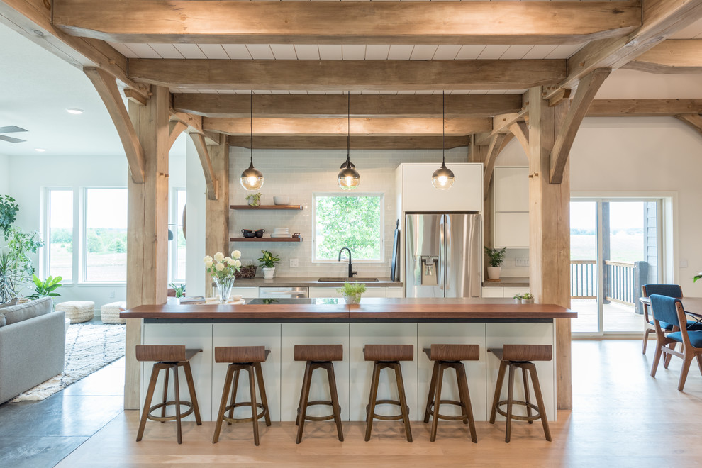 This is an example of a mid-sized country open plan kitchen in Minneapolis with flat-panel cabinets, white cabinets, concrete benchtops, with island, an undermount sink, white splashback, subway tile splashback, stainless steel appliances, grey benchtop, light hardwood floors and beige floor.