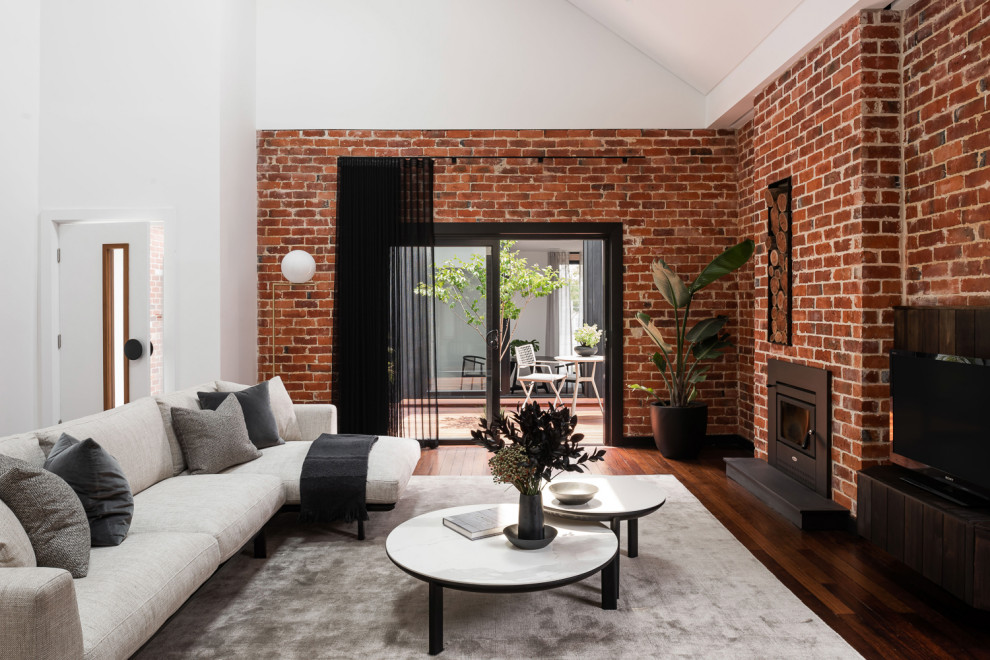 Пример оригинального дизайна: открытая гостиная комната среднего размера в стиле рустика с красными стенами, темным паркетным полом, печью-буржуйкой, фасадом камина из металла, коричневым полом и кирпичными стенами