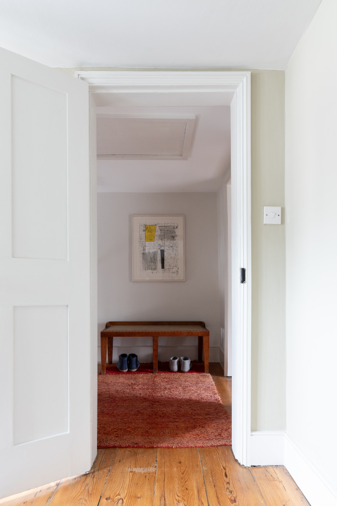 Foto på en liten hall, med vita väggar, mellanmörkt trägolv och vitt golv