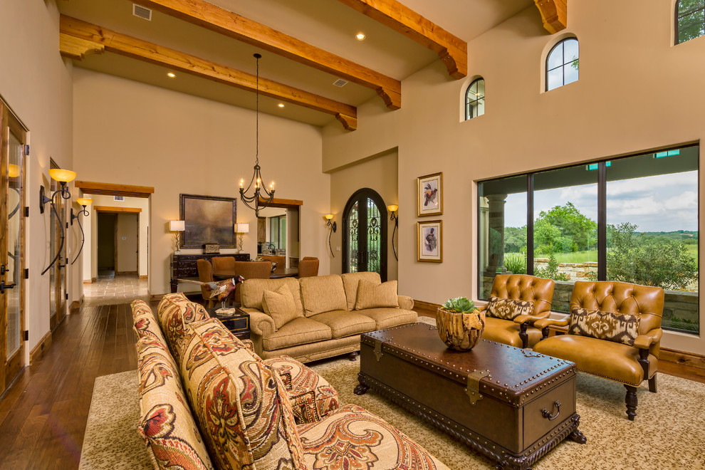 Photo of a large mediterranean open concept family room in Austin with beige walls, medium hardwood floors, a standard fireplace, a stone fireplace surround and a wall-mounted tv.