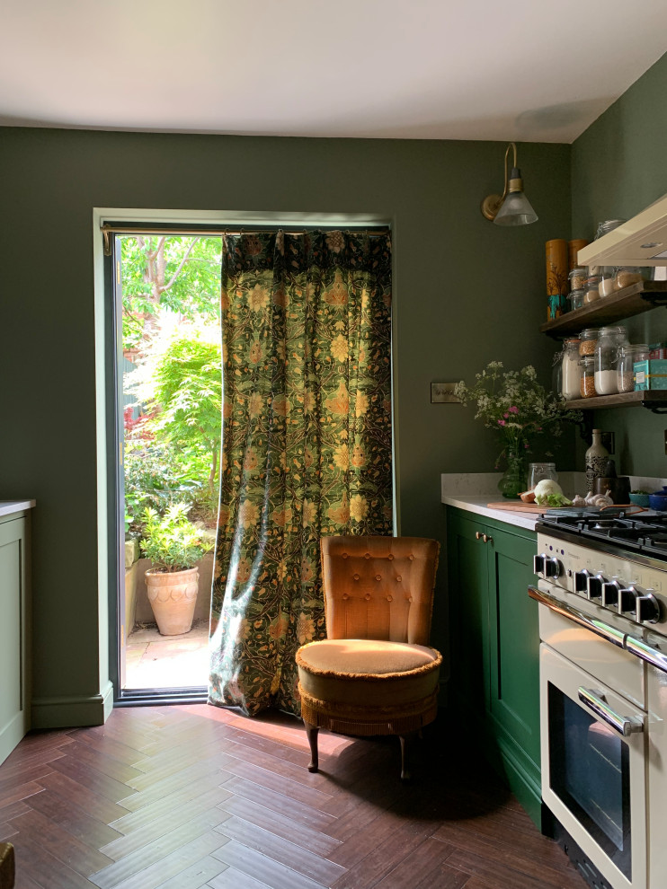 Photo of a small country enclosed kitchen in Other with a belfast sink, shaker cabinets, green cabinets, bamboo flooring, brown floors and a feature wall.