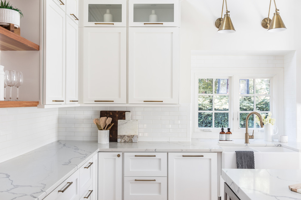 Eat-in kitchen - large transitional u-shaped light wood floor eat-in kitchen idea in Charlotte with a farmhouse sink, shaker cabinets, white cabinets, quartz countertops, white backsplash, ceramic backsplash, stainless steel appliances and an island