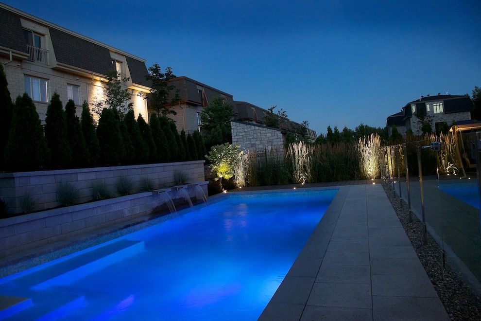 Ejemplo de casa de la piscina y piscina alargada actual de tamaño medio rectangular en patio trasero con losas de hormigón