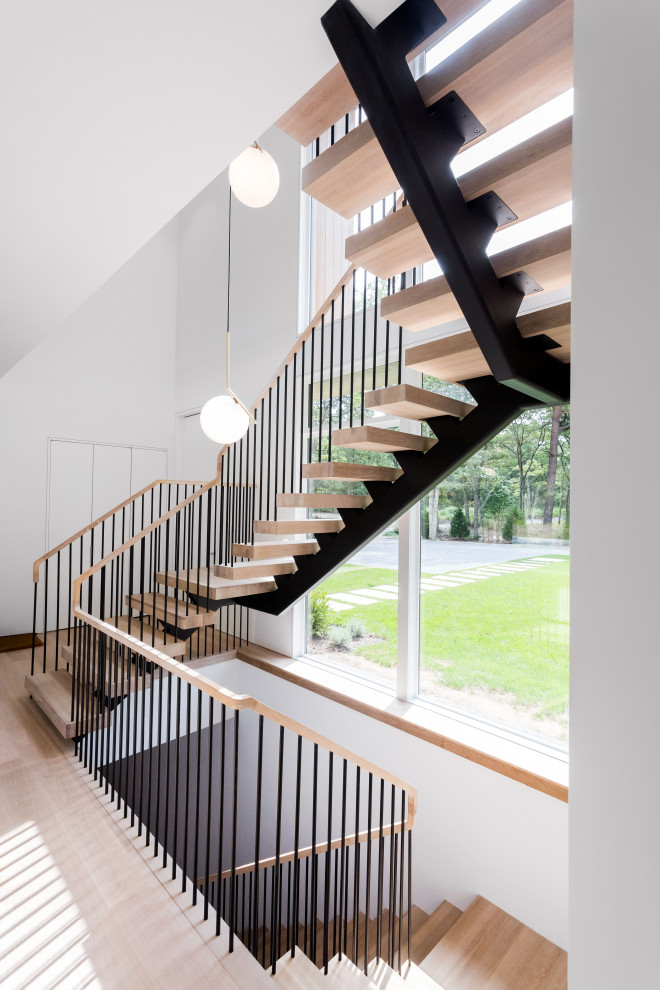 Large modern wood u-shaped staircase in New York with open risers and metal railing.