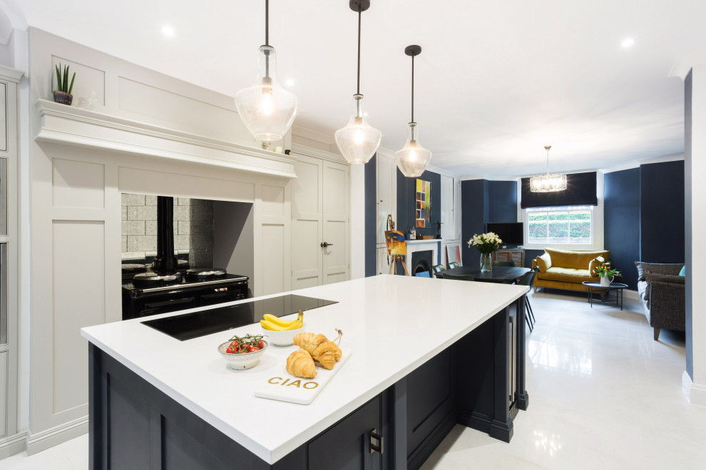 Large country u-shaped open plan kitchen in Hertfordshire with an integrated sink, beaded inset cabinets, grey cabinets, quartzite benchtops, metallic splashback, mirror splashback, black appliances, porcelain floors, with island, white floor and white benchtop.