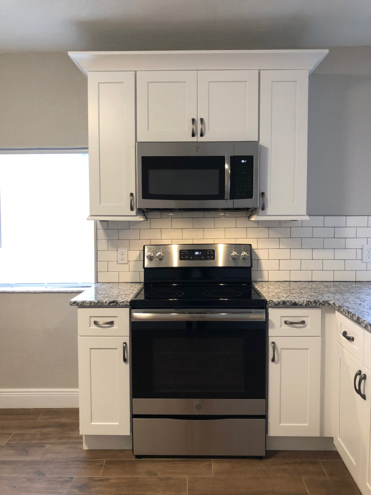 This is an example of a small arts and crafts l-shaped eat-in kitchen in Orlando with an undermount sink, shaker cabinets, white cabinets, granite benchtops, white splashback, subway tile splashback, stainless steel appliances, ceramic floors, with island, brown floor and grey benchtop.