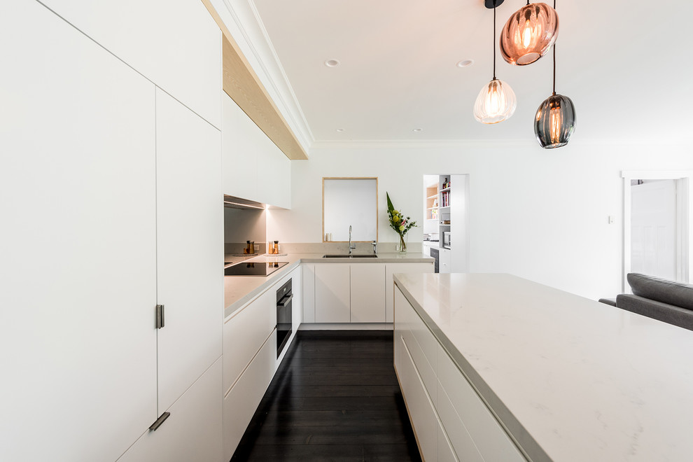 Photo of a large contemporary l-shaped open plan kitchen in Melbourne with an undermount sink, flat-panel cabinets, white cabinets, quartz benchtops, metallic splashback, mirror splashback, black appliances, dark hardwood floors, with island and brown floor.