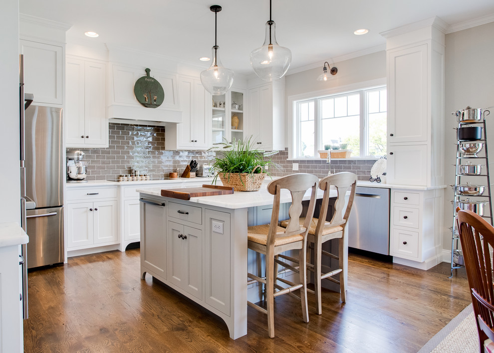 This is an example of a traditional eat-in kitchen in Other with shaker cabinets, white cabinets, grey splashback, subway tile splashback, stainless steel appliances, medium hardwood floors, with island and marble benchtops.