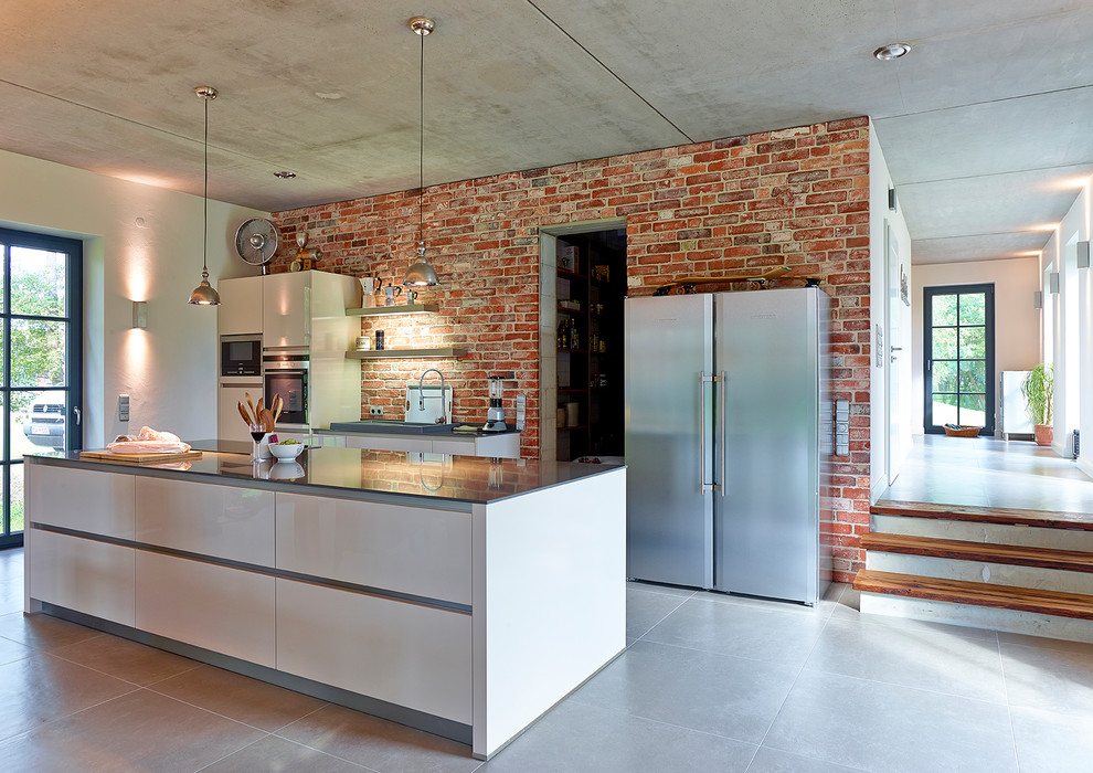 Inspiration for a large industrial galley eat-in kitchen in Hamburg with an integrated sink, flat-panel cabinets, white cabinets, solid surface benchtops, red splashback, stone slab splashback, stainless steel appliances, ceramic floors, with island, beige floor and black benchtop.