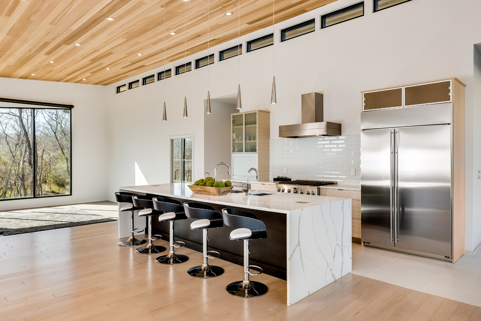 This is an example of an expansive modern single-wall open plan kitchen in Nashville with a triple-bowl sink, glass-front cabinets, light wood cabinets, marble benchtops, white splashback, subway tile splashback, stainless steel appliances, with island and white benchtop.