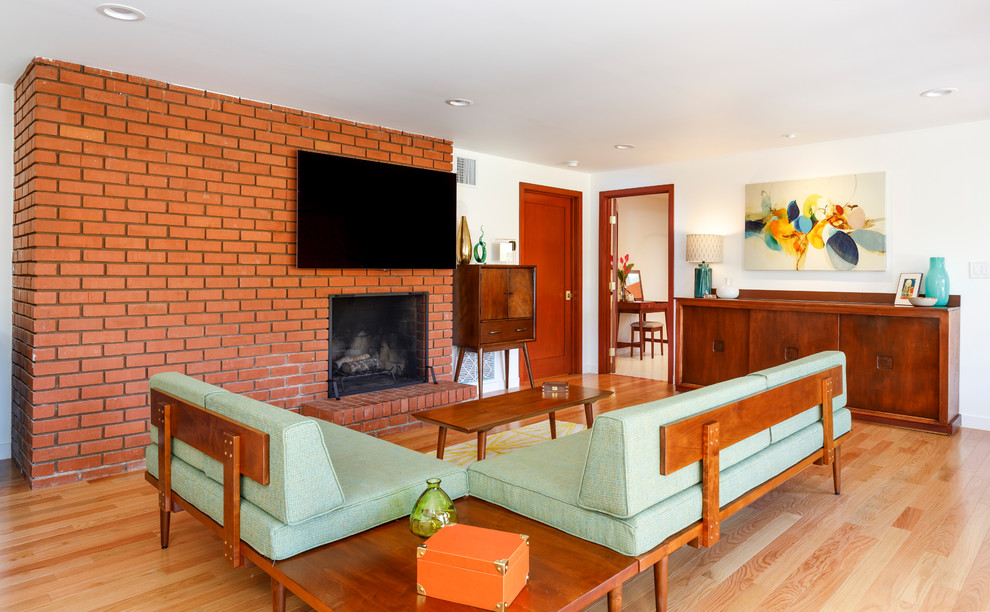 Photo of a midcentury living room in Los Angeles with white walls, light hardwood floors, a standard fireplace, a brick fireplace surround, a wall-mounted tv and beige floor.