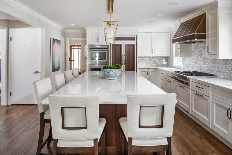 This is an example of a large transitional l-shaped kitchen in Detroit with white cabinets, quartz benchtops, panelled appliances, dark hardwood floors, with island, brown floor, shaker cabinets, multi-coloured splashback and white benchtop.