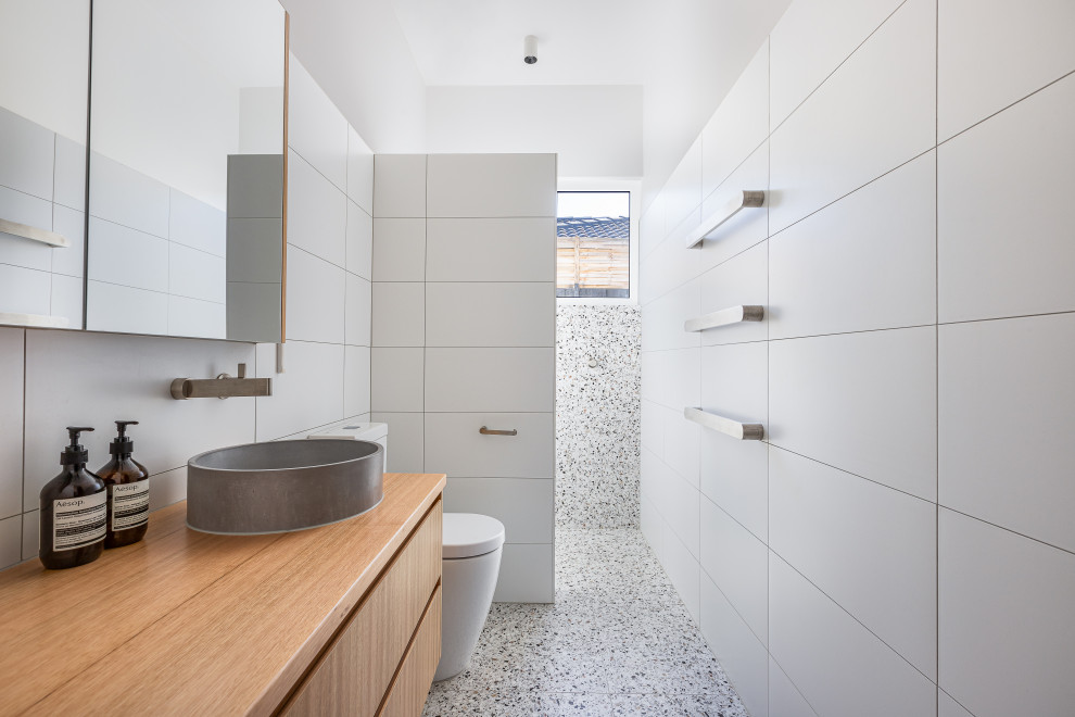 Contemporary bathroom in Melbourne with flat-panel cabinets, medium wood cabinets, a built-in shower, white tiles, a vessel sink, wooden worktops, grey floors, brown worktops, a single sink and a floating vanity unit.