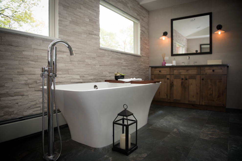 Photo of a large modern master bathroom in Other with shaker cabinets, medium wood cabinets, a freestanding tub, a corner shower, a one-piece toilet, white tile, stone tile, white walls, slate floors, a drop-in sink, solid surface benchtops, black floor, a hinged shower door and grey benchtops.
