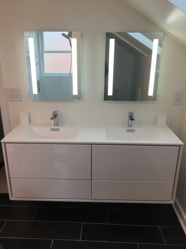 This is an example of a large modern master bathroom in Charlotte with slate floors, an integrated sink, black floor, flat-panel cabinets, white cabinets, an alcove shower, a two-piece toilet, white tile, subway tile, white walls, glass benchtops, a hinged shower door and white benchtops.