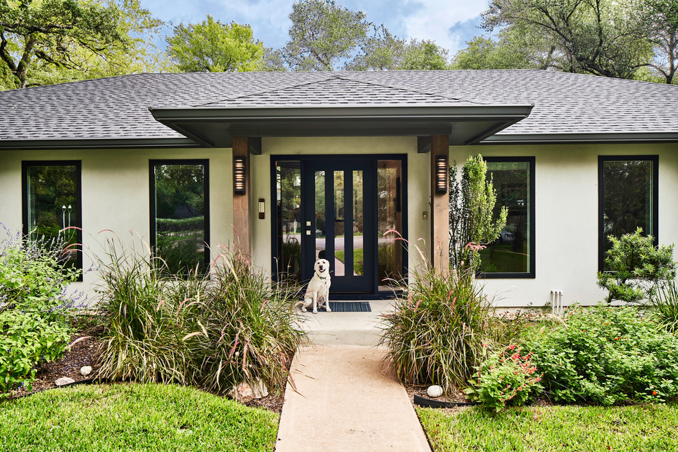 This is an example of a large midcentury one-storey stucco grey house exterior in Austin with a hip roof and a shingle roof.