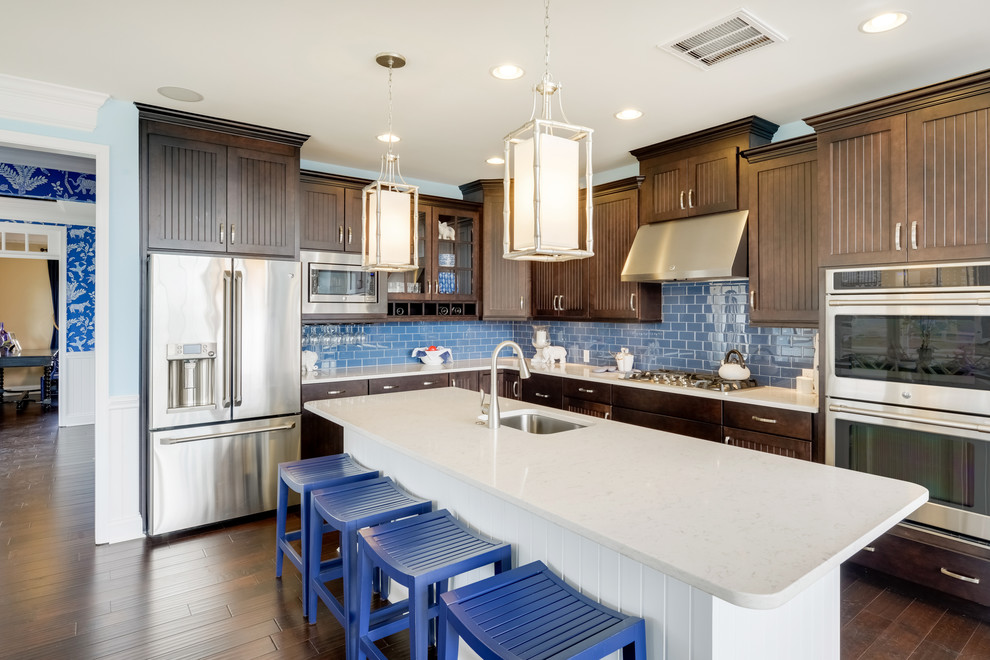 Photo of a beach style l-shaped kitchen in Other with an undermount sink, dark wood cabinets, blue splashback, subway tile splashback, stainless steel appliances, dark hardwood floors, with island and brown floor.